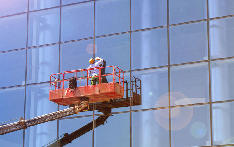 Profissional trabalha em altura para remover manchas na fachada de vidro